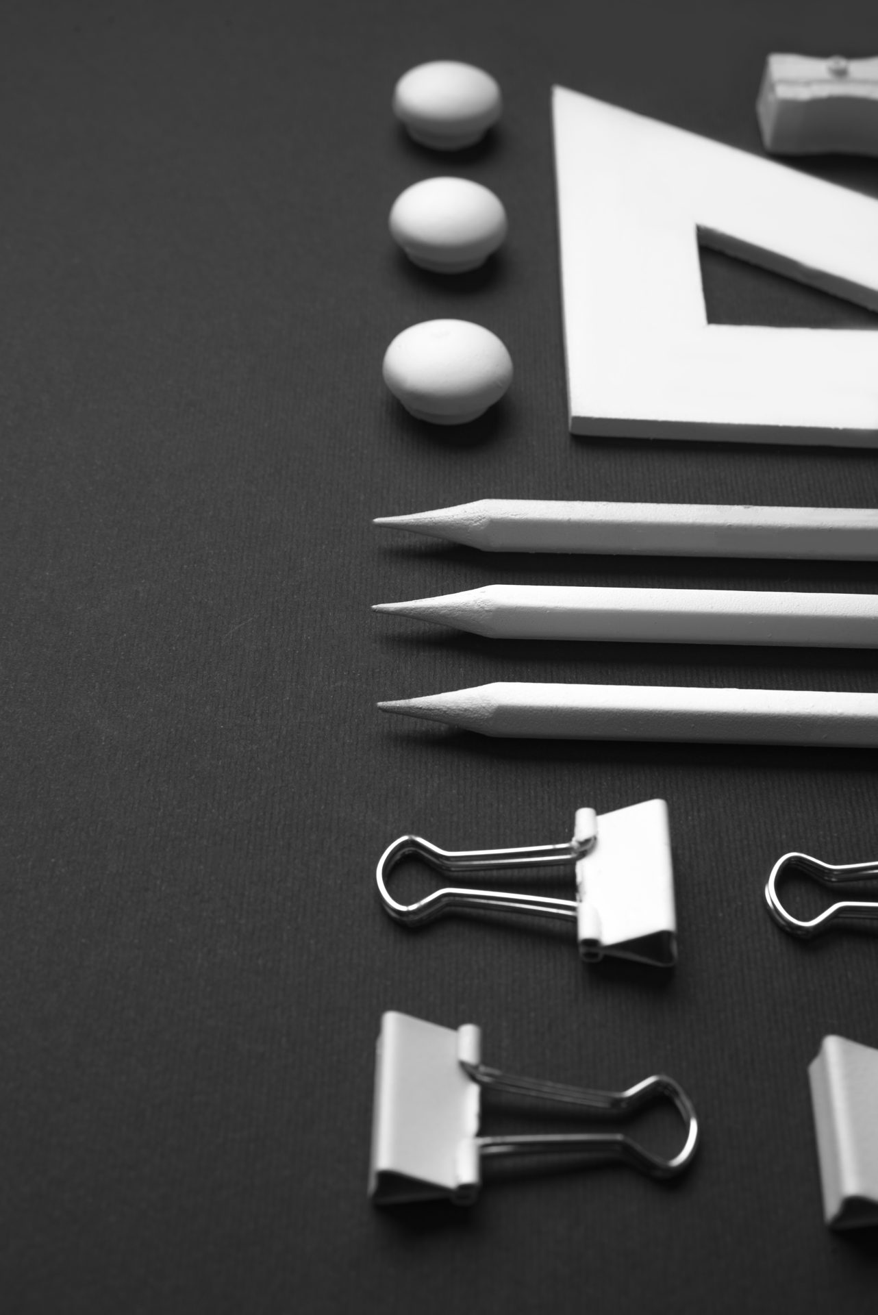 Pencils, binder clips and a set square laid out on dark paper