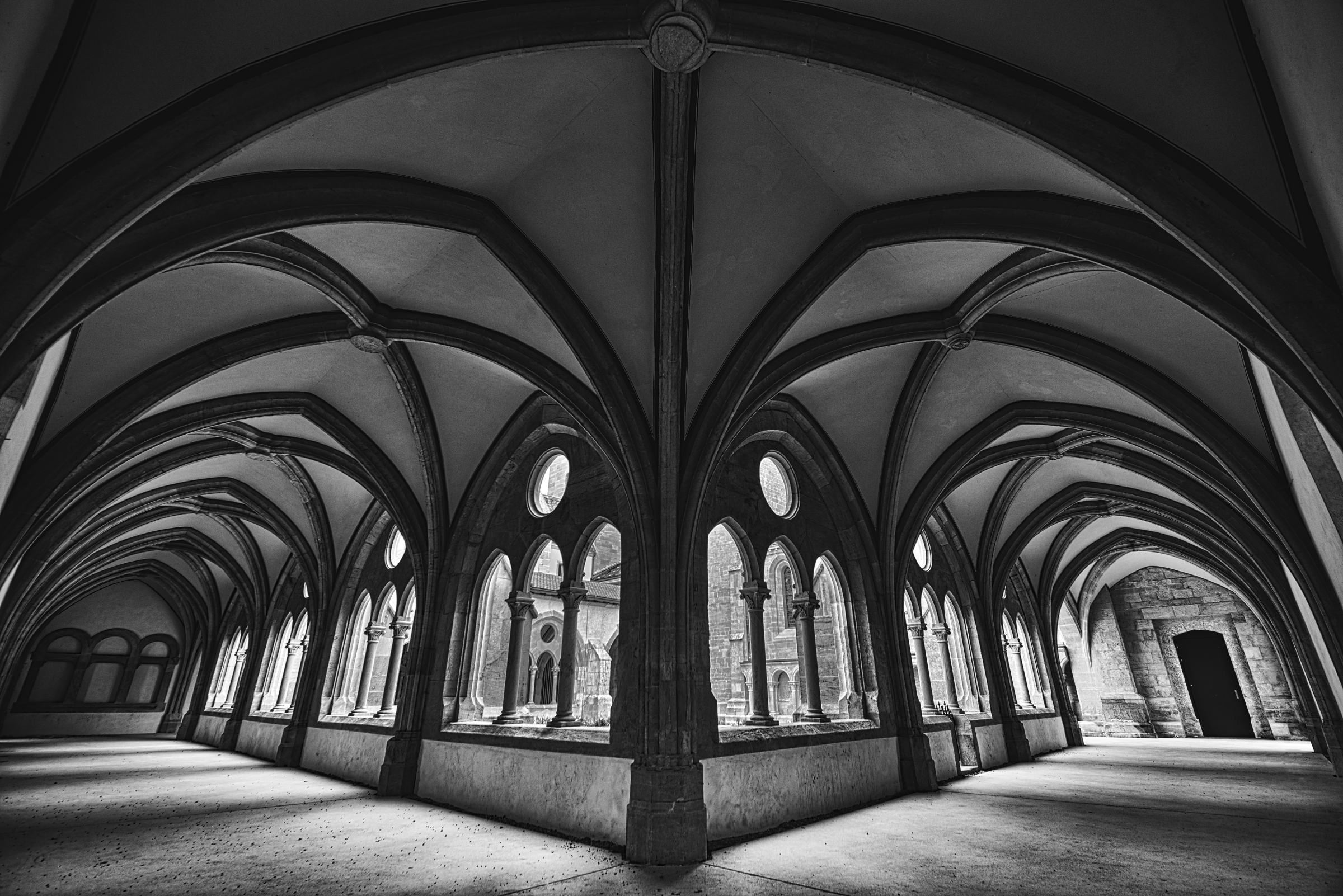 A vaulted stone cloister with arched windows onto a courtyard